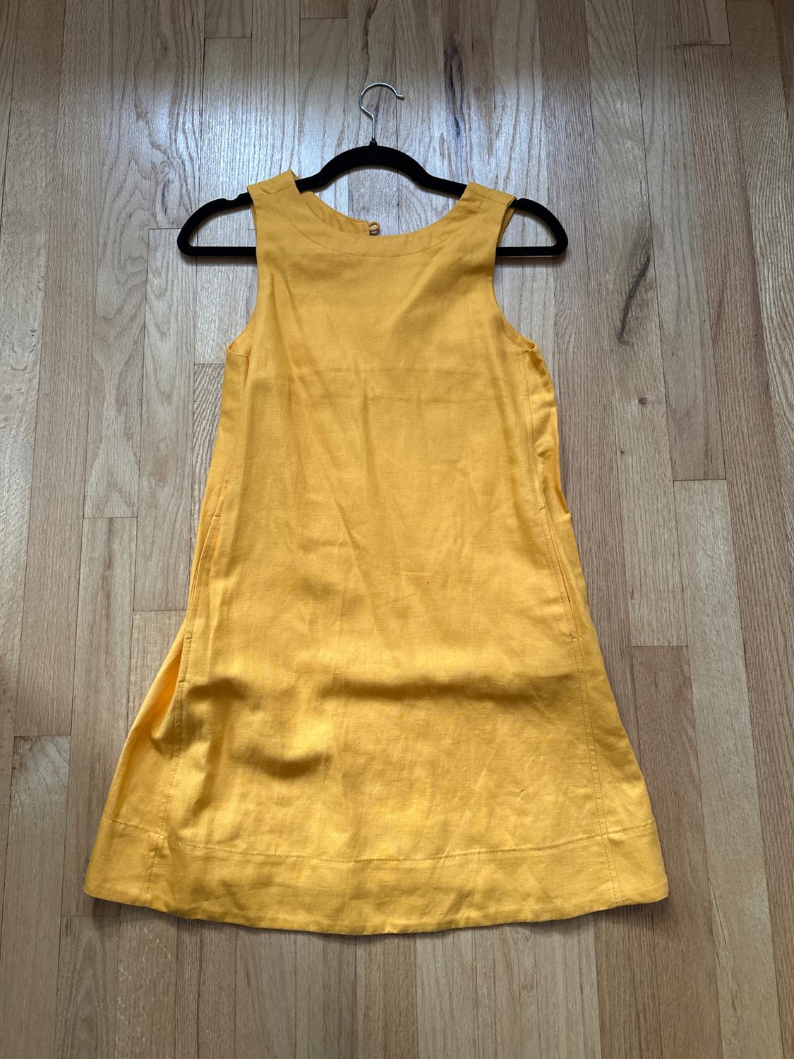 Sleeveless yellow dress hanging on a black hanger over a light wood floor.