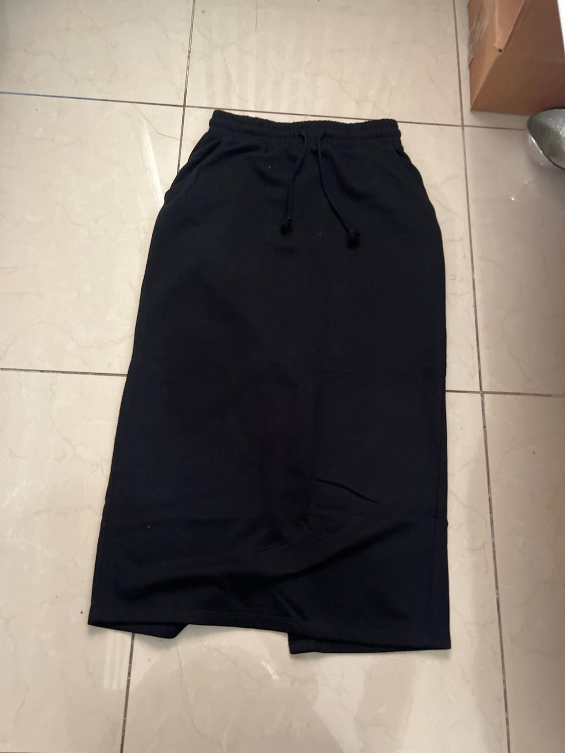 Long black skirt with lacing at the waist, laid out on a light tiled floor.