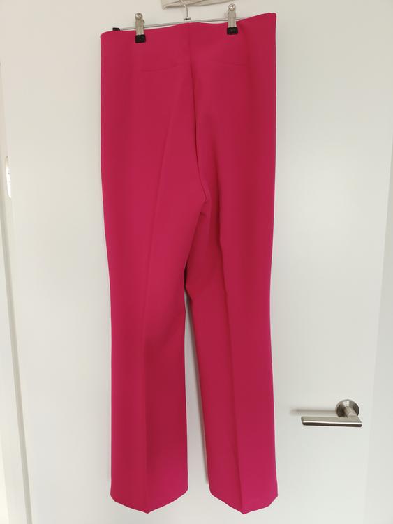 Fuchsia trousers hanging on a hanger over a white door.