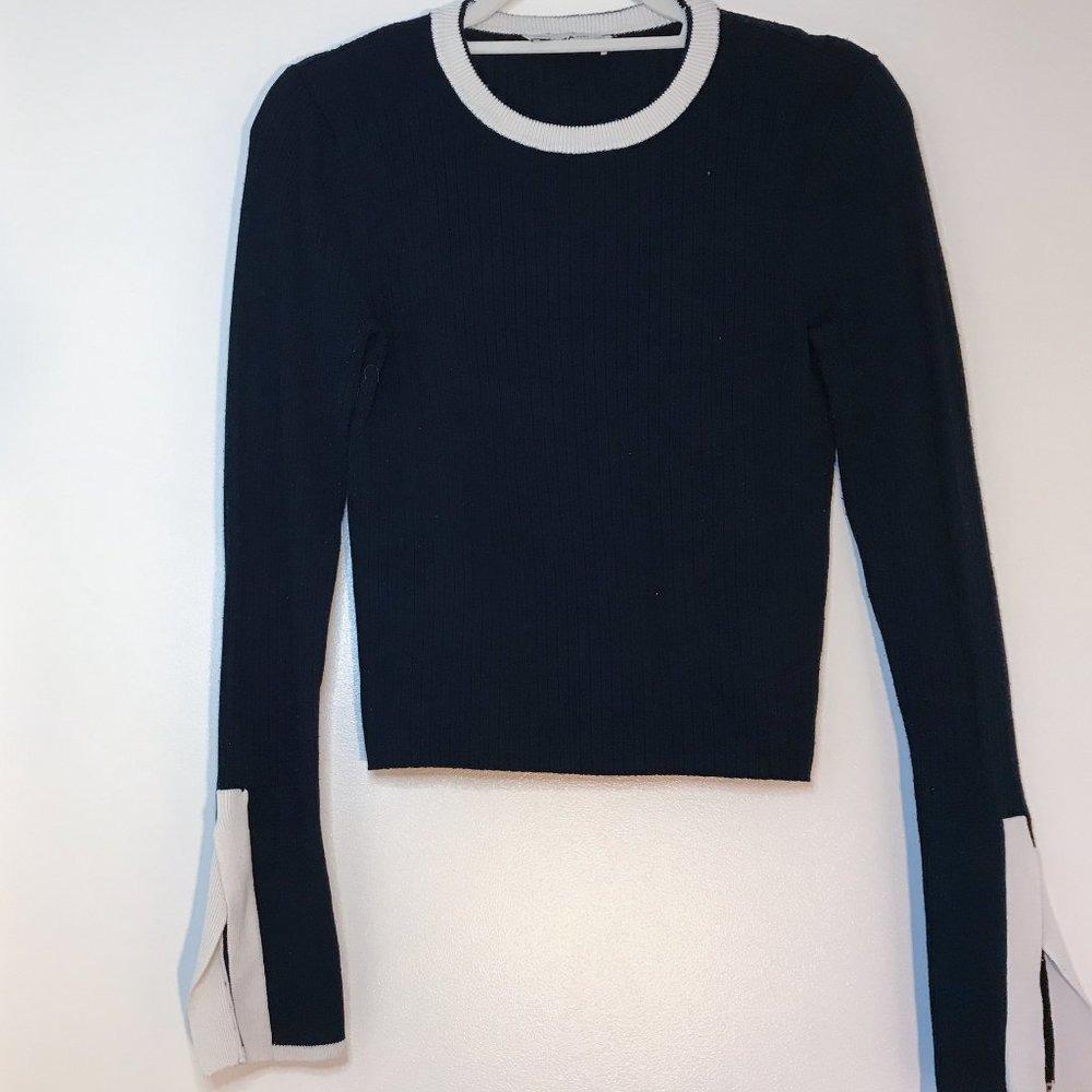 A black long-sleeve sweater with a ribbed texture, a white crew neck, and white cuffs with slits, hanging on a hanger.