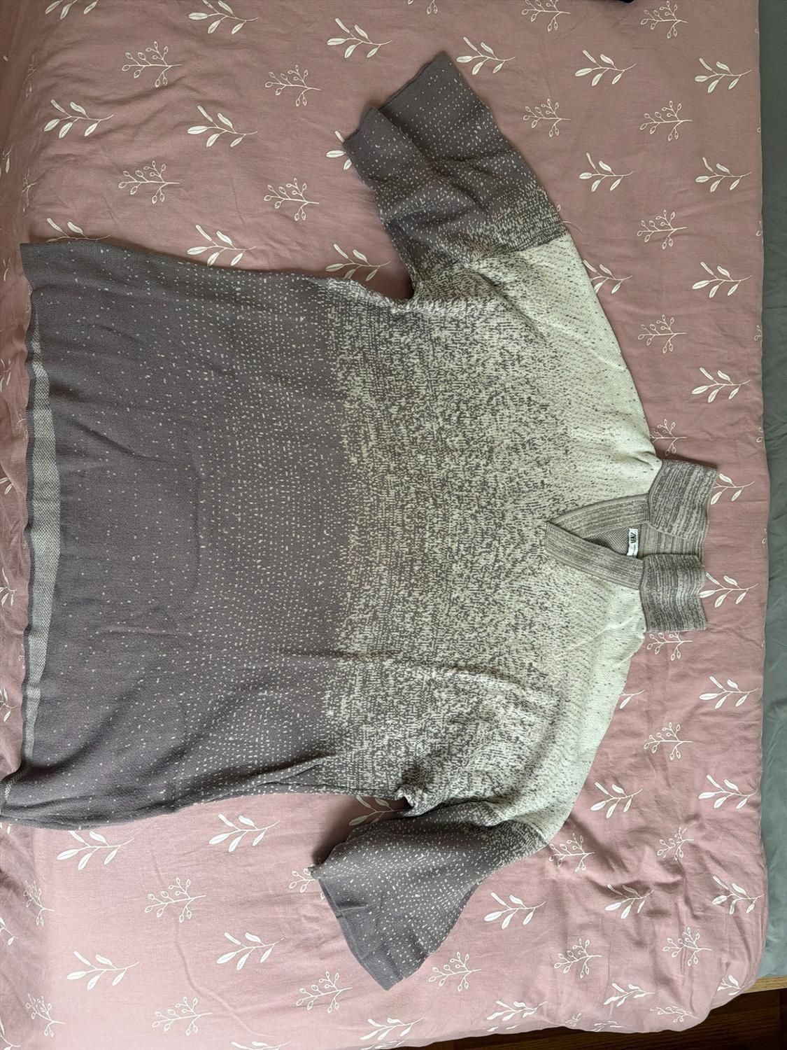 Heathered gradient sweater fading from gray to cream with a V-neck,
laid out on a pink sheet with a white leaf print.