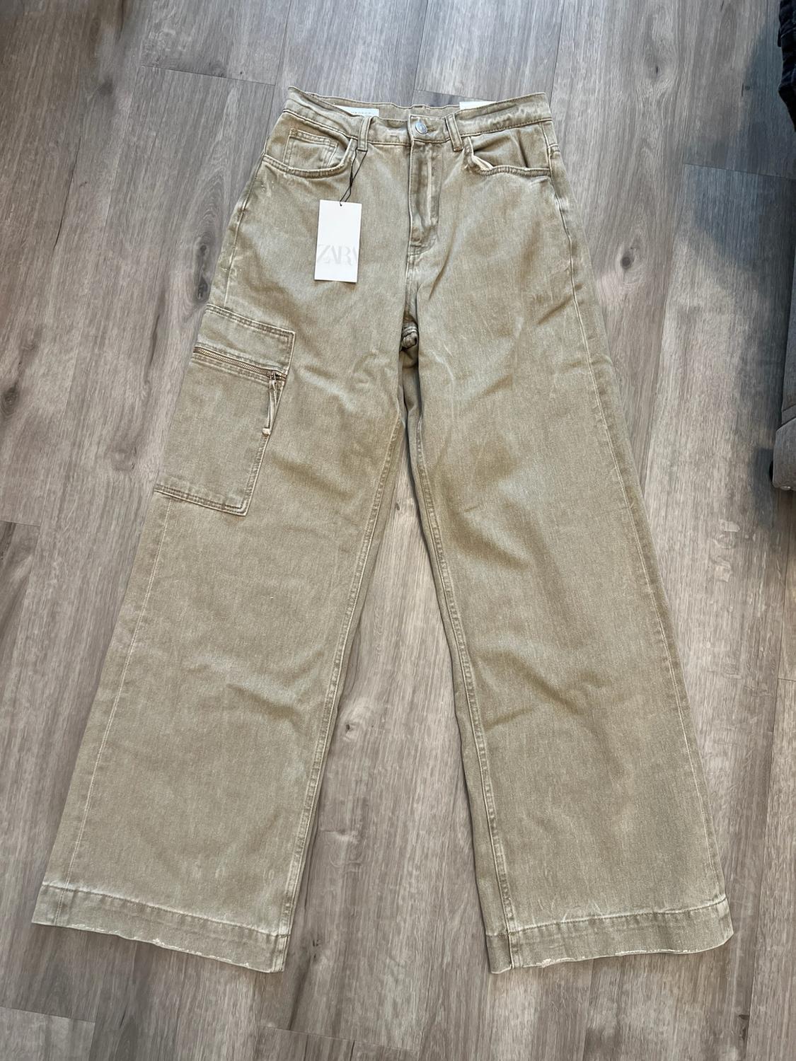 Wide khaki cargo-pocket jeans laid out on a wooden floor. Label with the text ZARA.