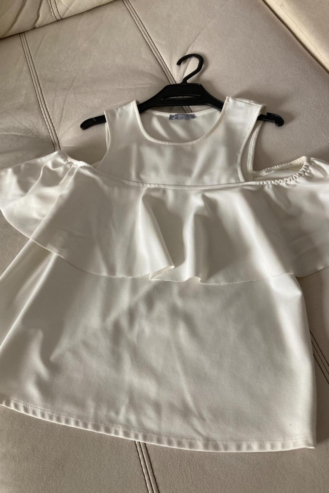 Front view of a white sleeveless blouse with ruffles on the neckline and off-the-shoulder design.