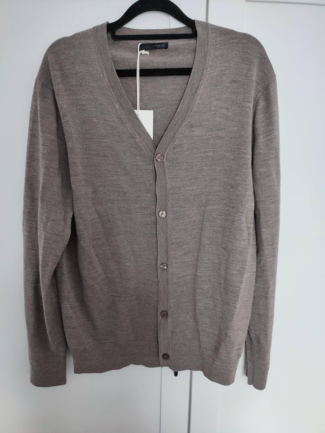 Long-sleeved brown knitted V-neck cardigan with buttons, hanging on a black hanger on a white door.