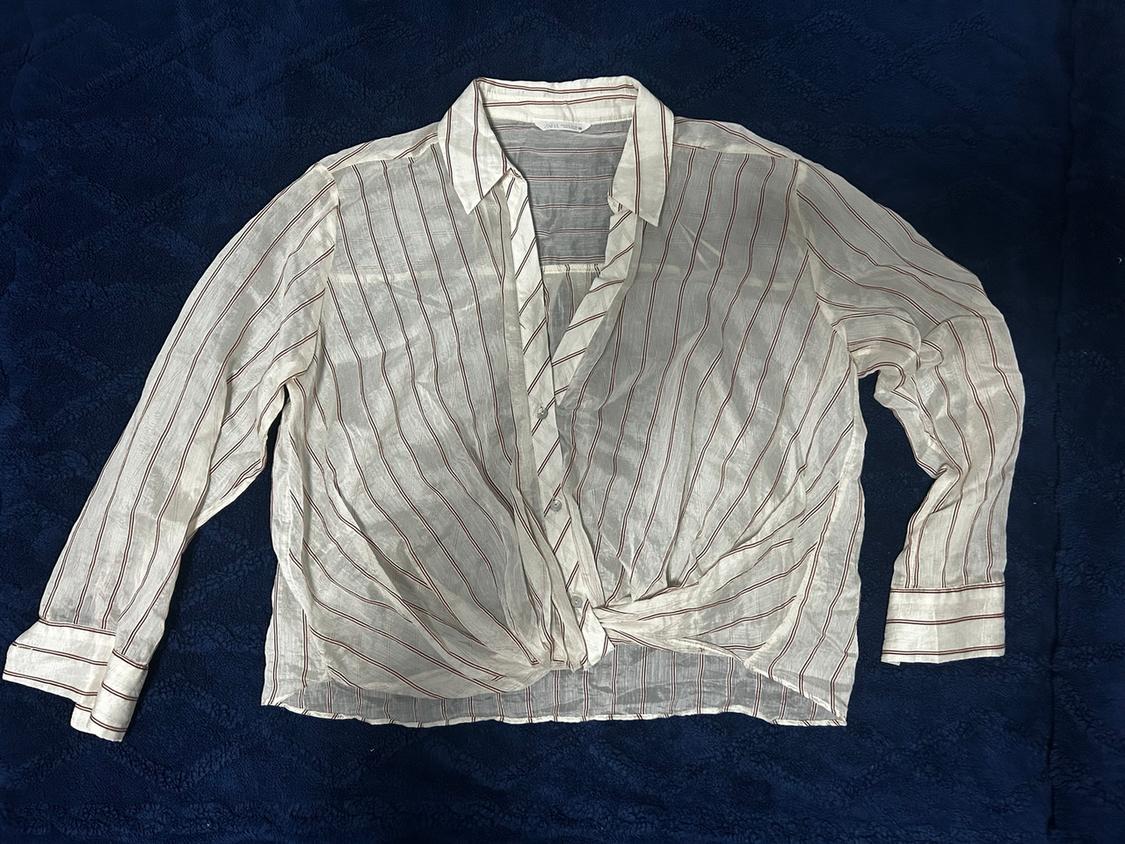 Vertical striped shirt in light tones with a front knot, on a dark blue background. Long sleeves and classic collar.