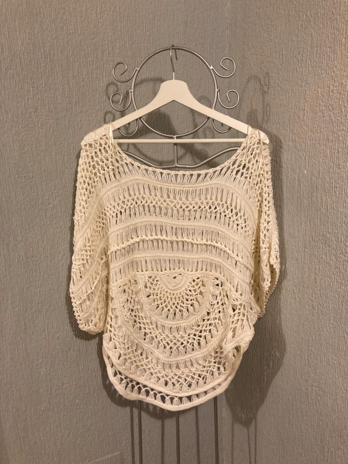 Front view of a beige crochet blouse with a circular design and short sleeves.