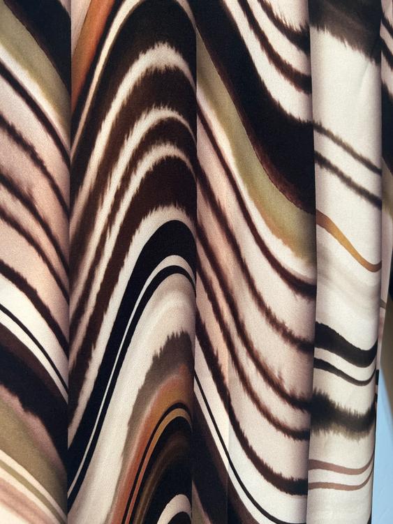 Fabric with a wave pattern in brown, beige, and black tones, creating a dynamic and fluid visual effect.
