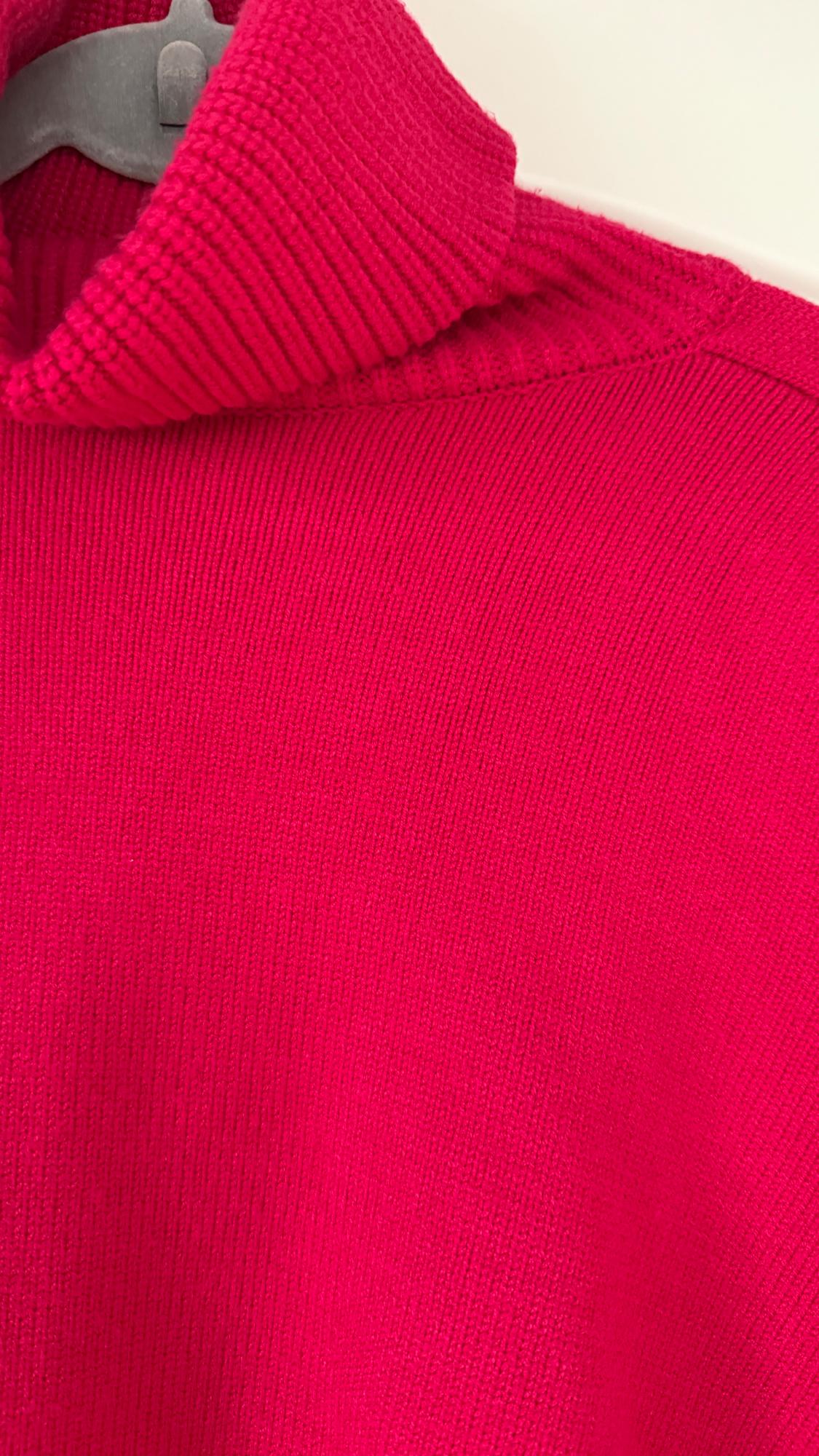 Close-up of a red knitted roll-neck jumper, hanging on a grey hanger against a white background.