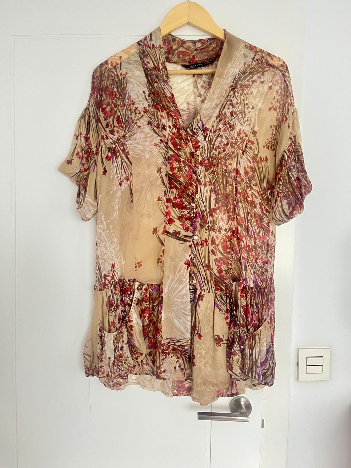 Beige blouse with red and brown floral print, hanging on a wooden hanger over a white door.
