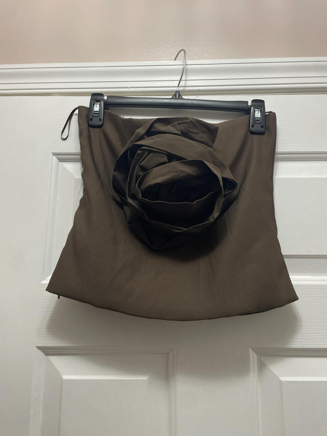 Brown strapless top with a large decorative flower in the center, hanging on a black hanger on a white door.