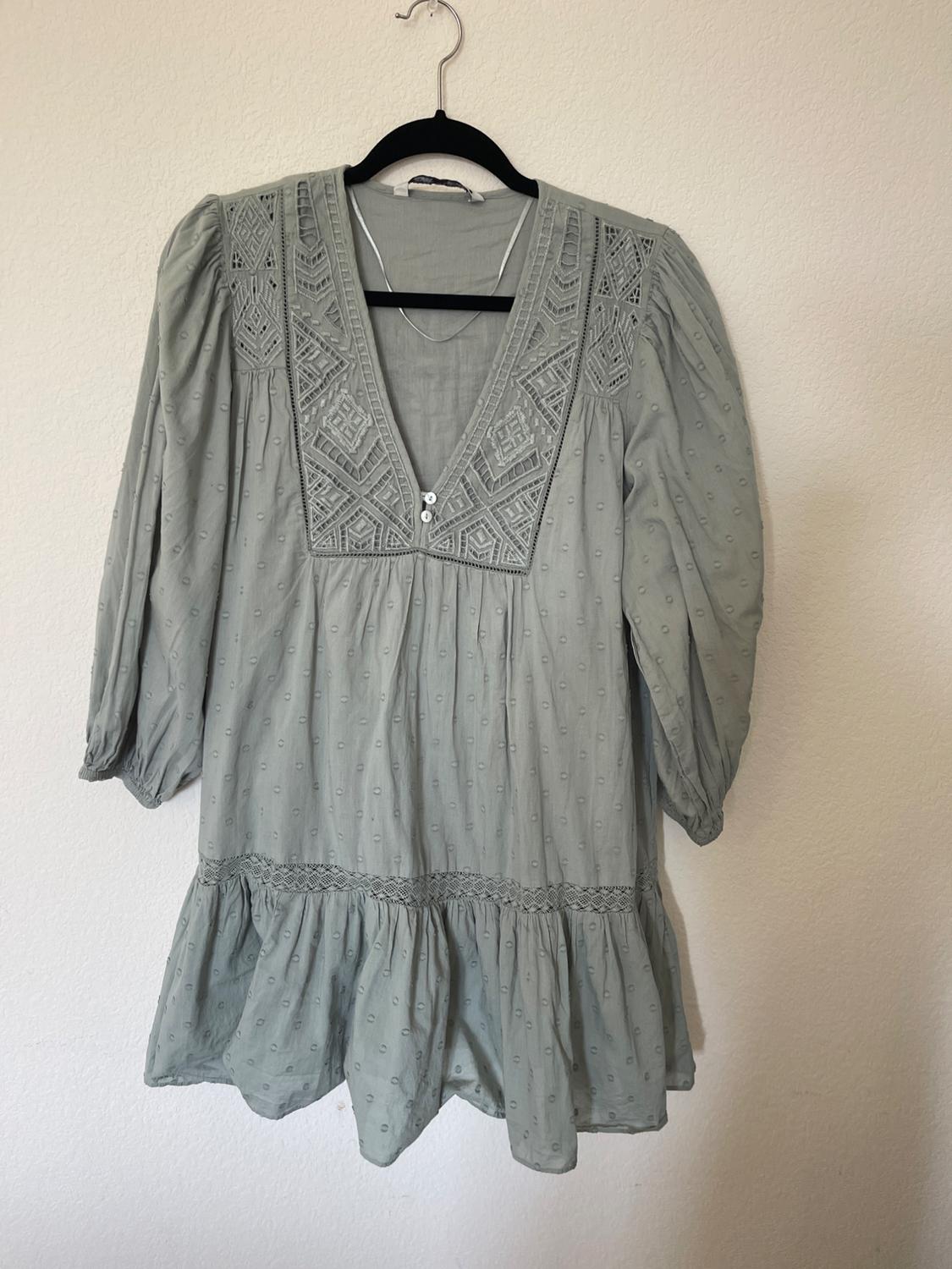 Light green blouse with geometric embroidery at the neckline and puff sleeves, hanging on a black hanger against a white background.