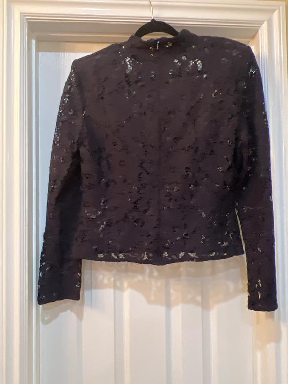 Black lace jacket hanging on a hanger over a white door. Elegant design with sheer details.