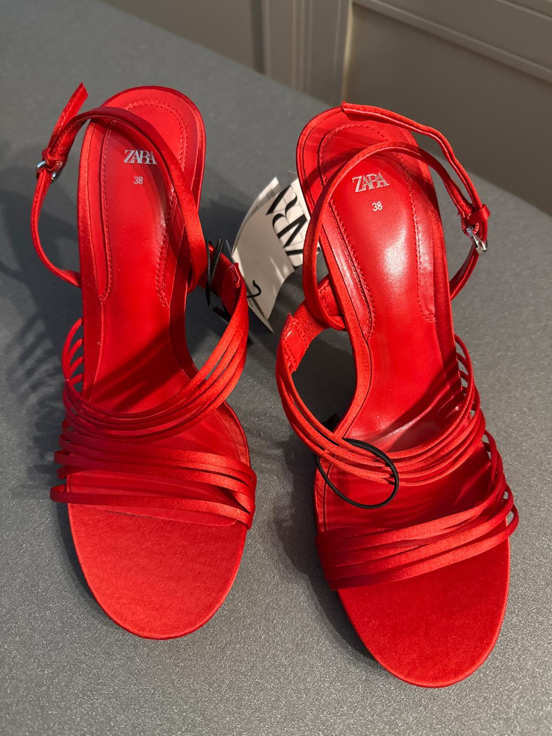 Red high-heeled sandals with thin straps and buckle, ZARA brand, size 38, on a gray surface. Visible tag.