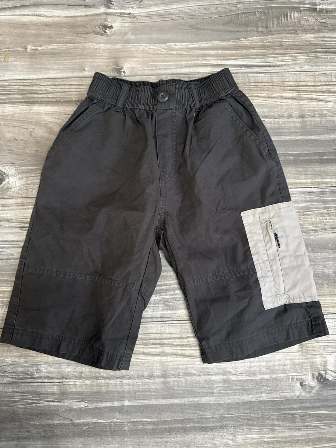 Dark grey shorts with an elasticated waistband and button. Includes a light grey cargo pocket with a zip, against a wooden background.