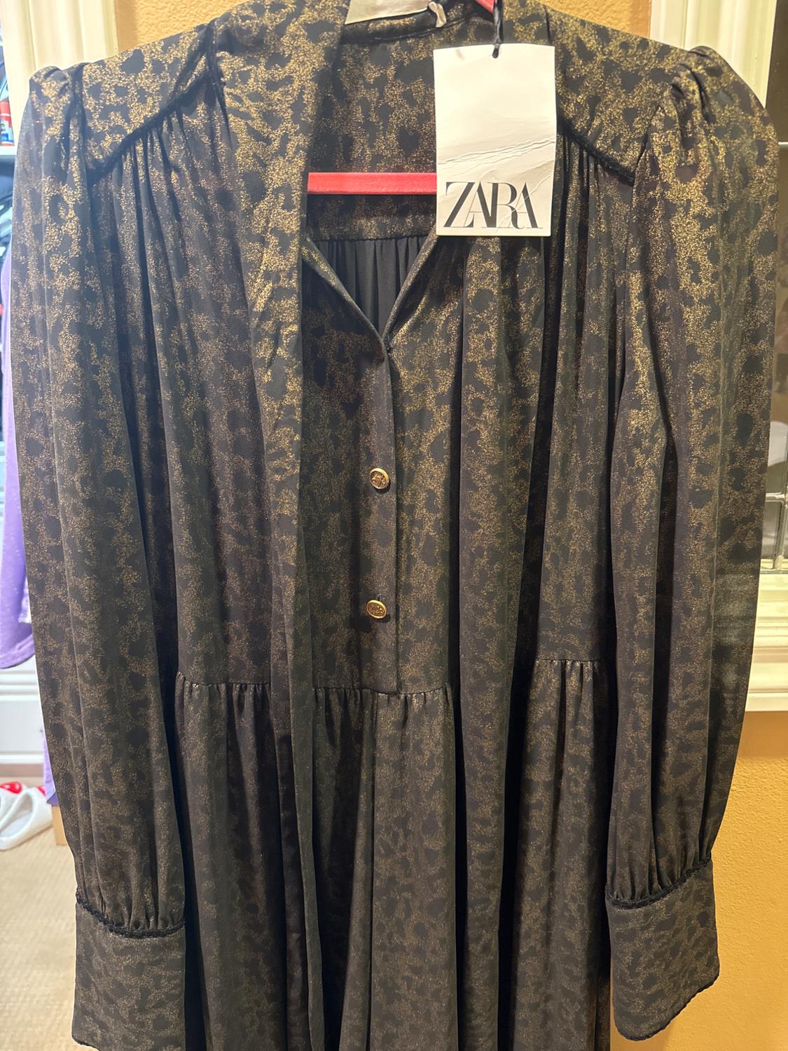 Long dress with dark print hanging on a hanger. Visible label with the text "ZARA". Store interior background.