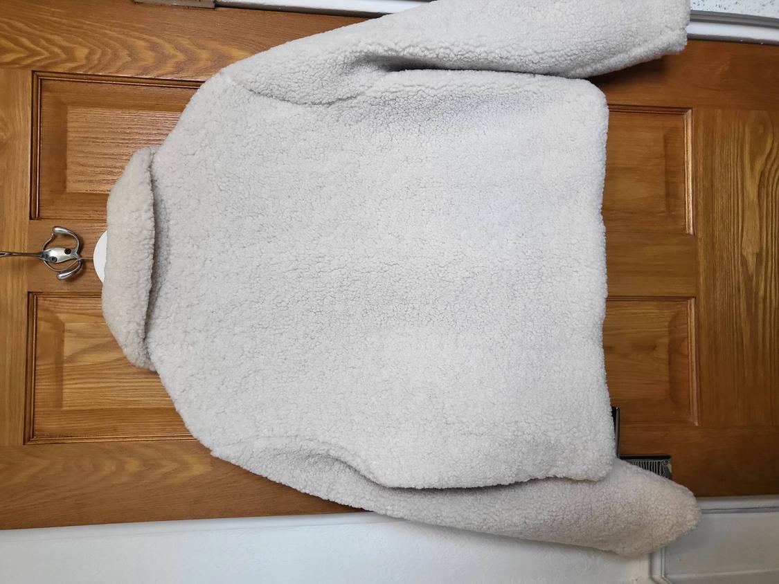 White wool jacket hanging on a wooden door. The texture is fluffy and warm, ideal for winter.
