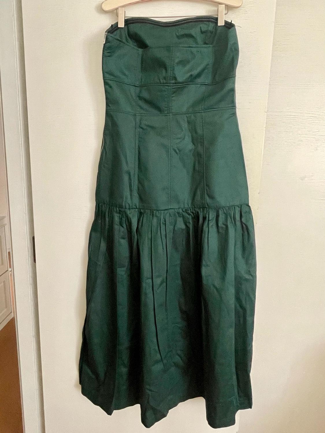 Dark green strapless dress with a fitted bodice and gathered skirt, hanging on a wooden hanger against a white door.