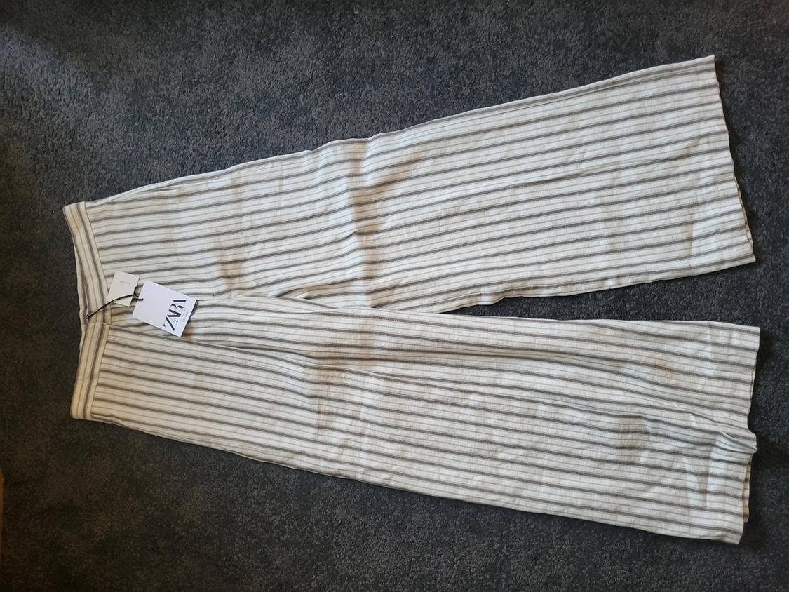 White and grey striped trousers on a grey rug, with a visible label that reads "ZARA".