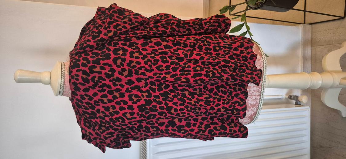 Animal print blouse in red and black on a white mannequin, with a light wall background and a decorative plant.