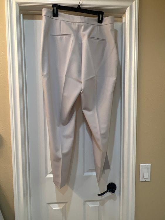 Beige pants hanging on a white door with a black hanger. Indoor setting with cream-colored walls.