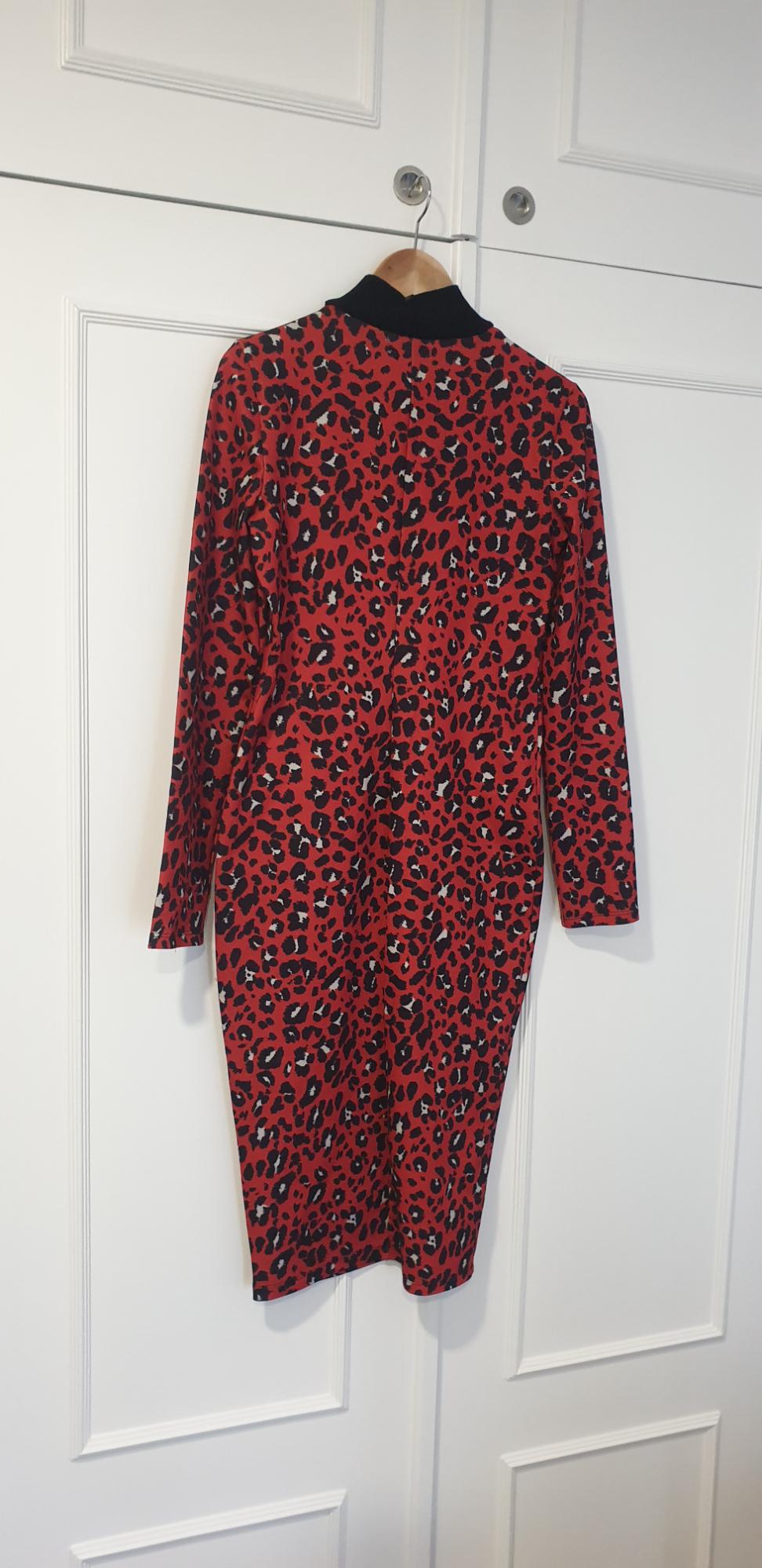 Red dress with black leopard print and a high neck, hanging on a wooden hanger in front of a white wardrobe.