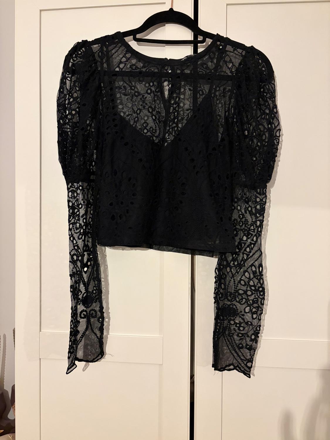 Black lace blouse with long sleeves and floral details, hanging on a black hanger in front of a white wardrobe.