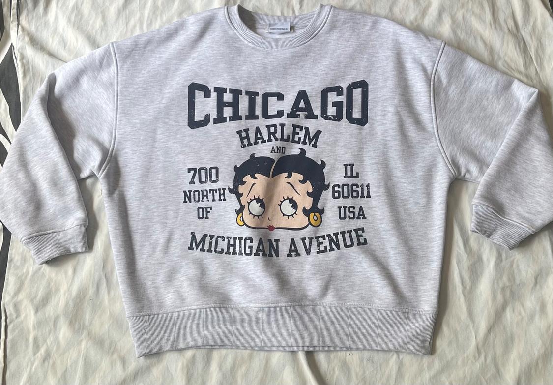 Light gray sweatshirt on fabric featuring a Betty Boop drawing and the text: CHICAGO HARLEM AND 700 NORTH OF IL 60611 USA MICHIGAN AVENUE.