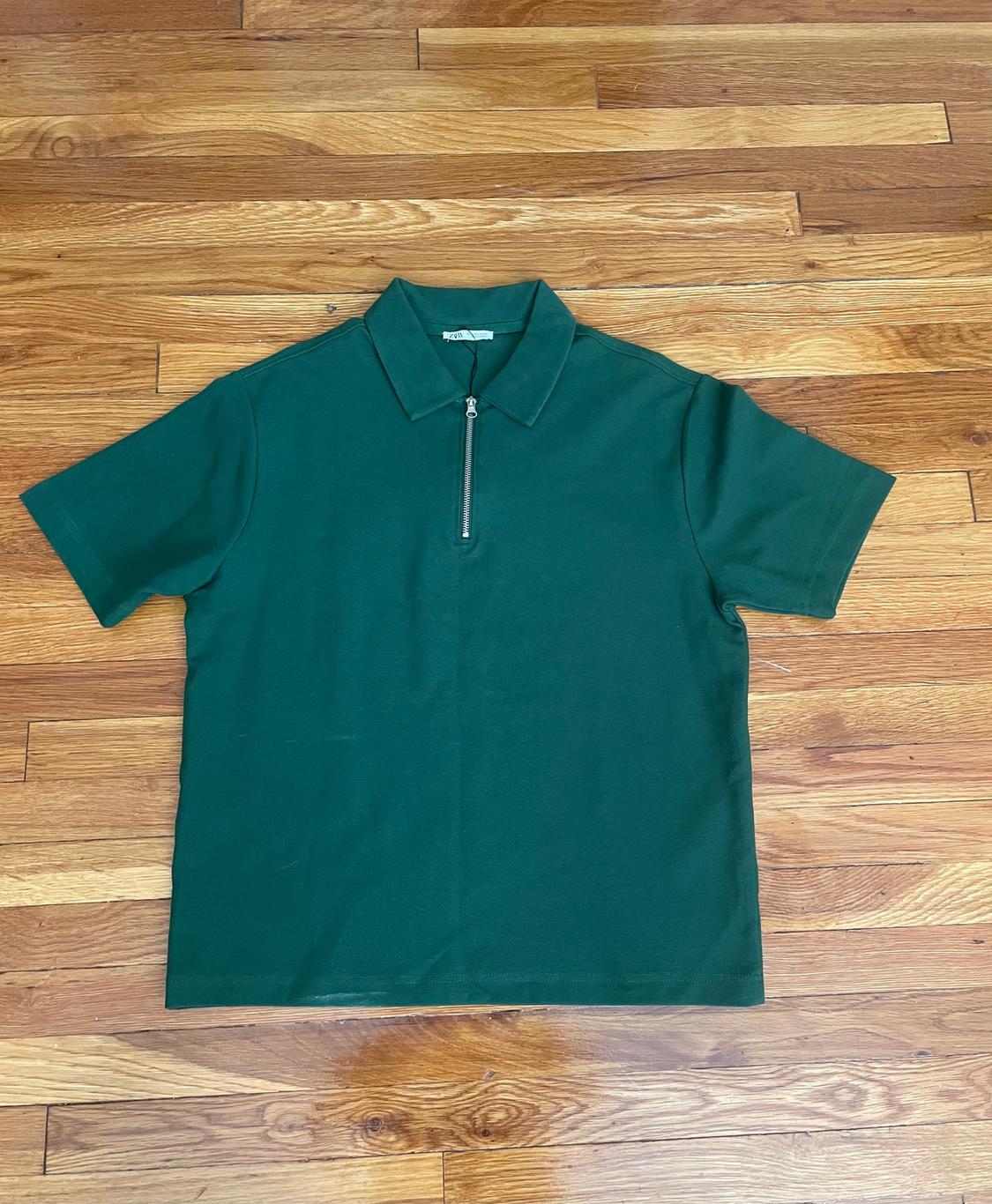Green polo shirt with a zip-up chest, on a wooden floor.