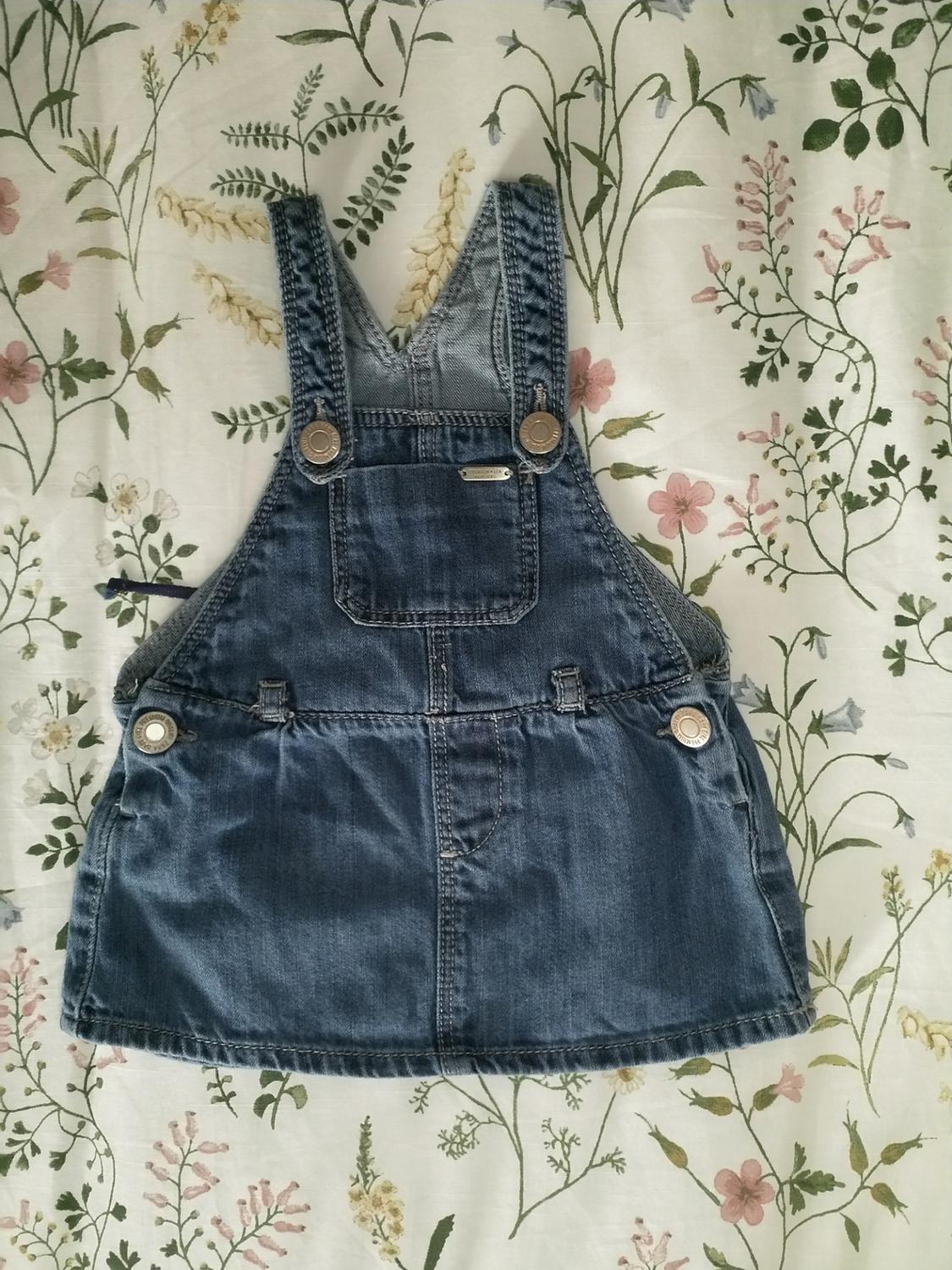 Front view of blue denim dungarees with a front pocket and metal buttons.