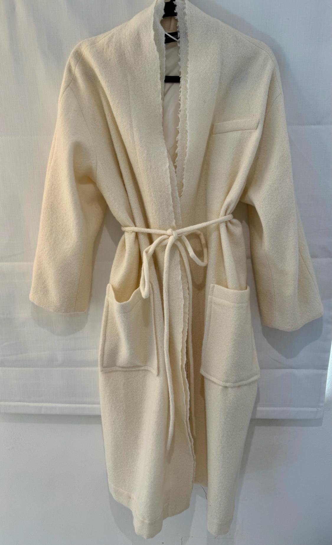 Cream-coloured wrap-style coat hanging on a black hanger against a white background. Features a belted waist, pockets, and frayed edges.