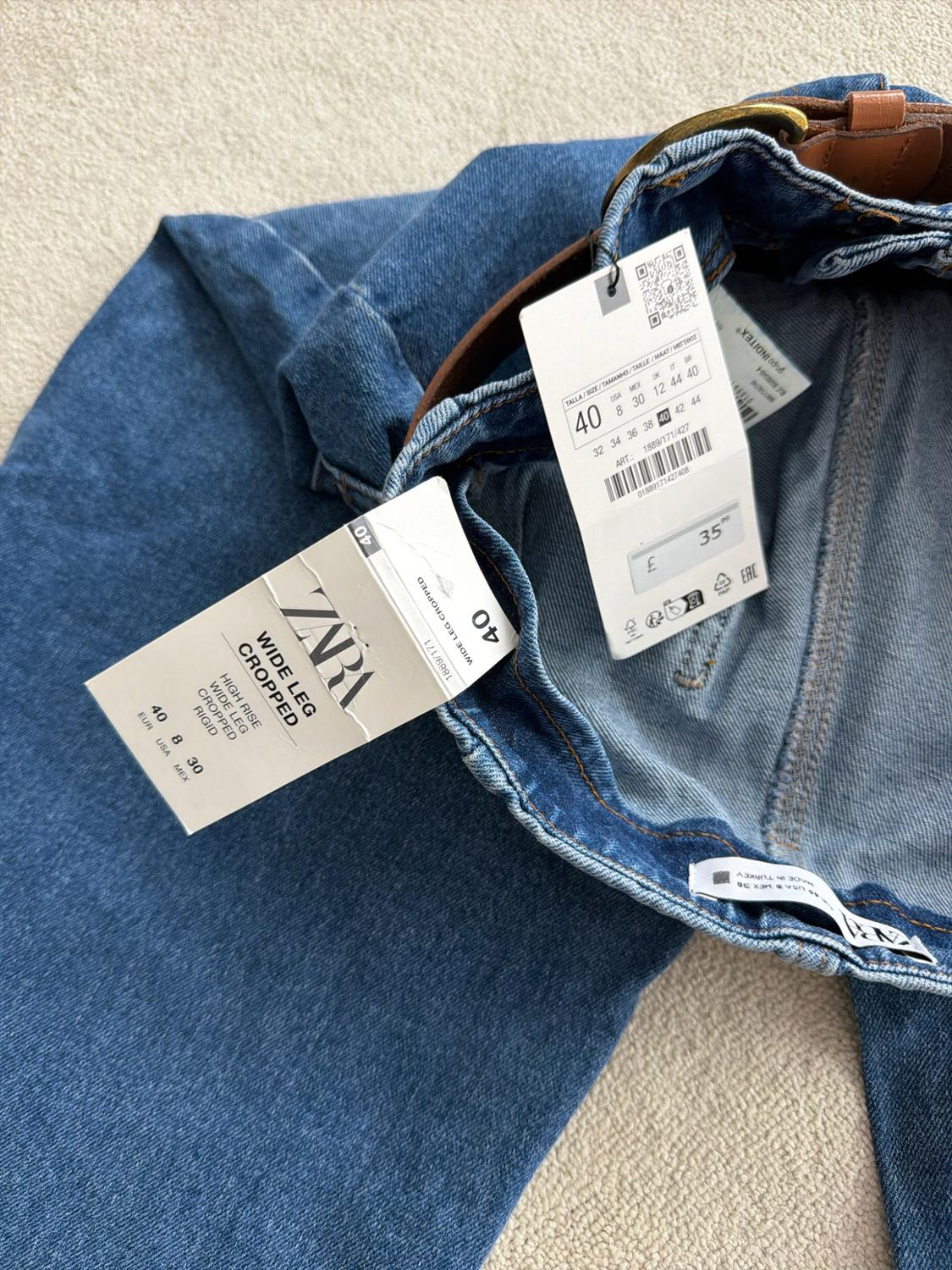 Blue jeans with a brown belt. Visible text: ZARA WIDE LEG CROPPED HIGH RISE RIGID 40 EUR 8 USA 30 MEX £ 35.99.