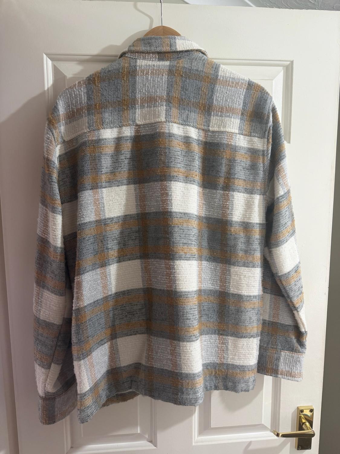 Rear view of a grey, white, and mustard check casual shirt, hanging on a hanger over a white door.