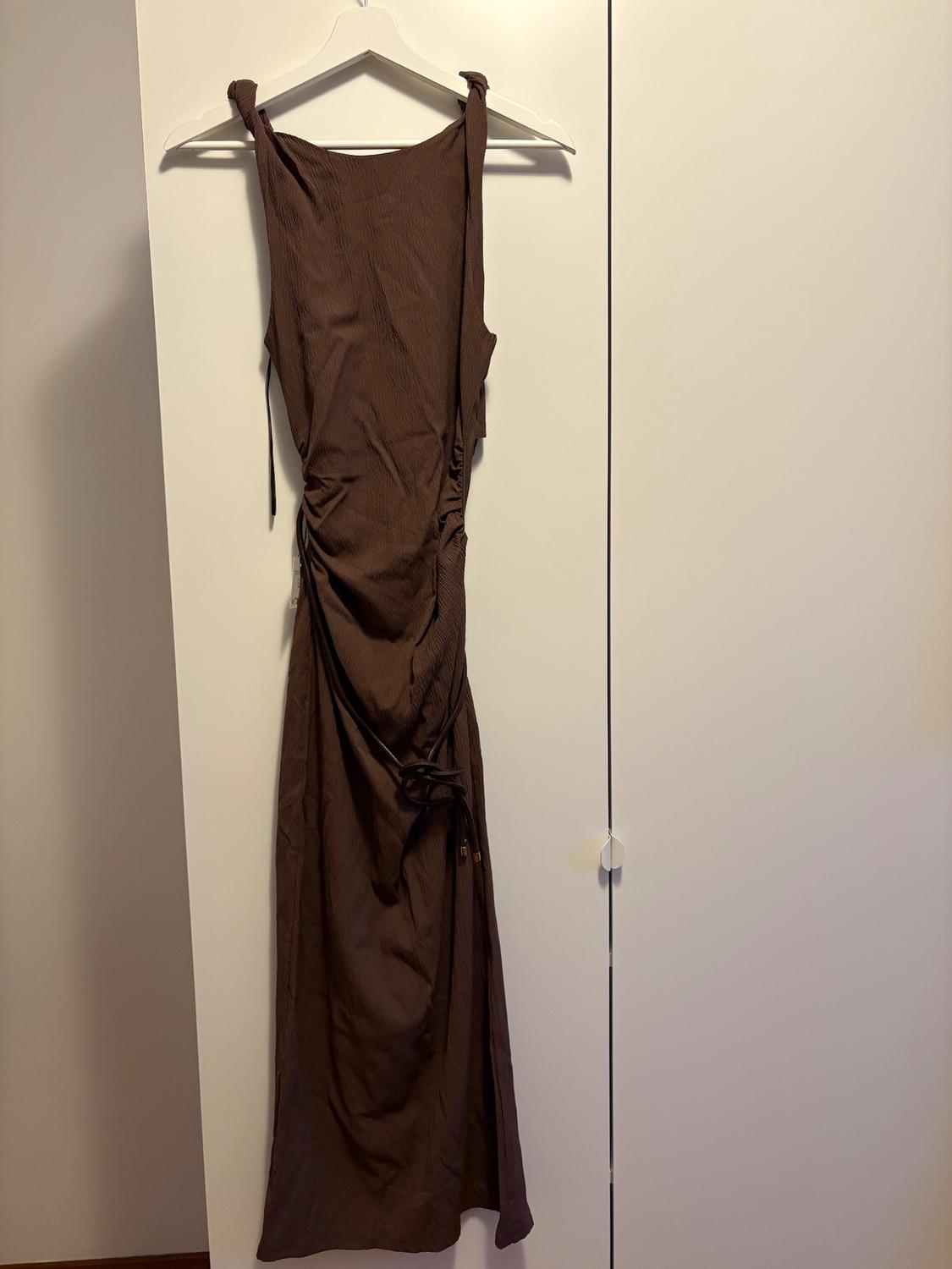 Sleeveless brown dress hanging on a white hanger in front of a white wardrobe. Fitted design with side ruching detail.