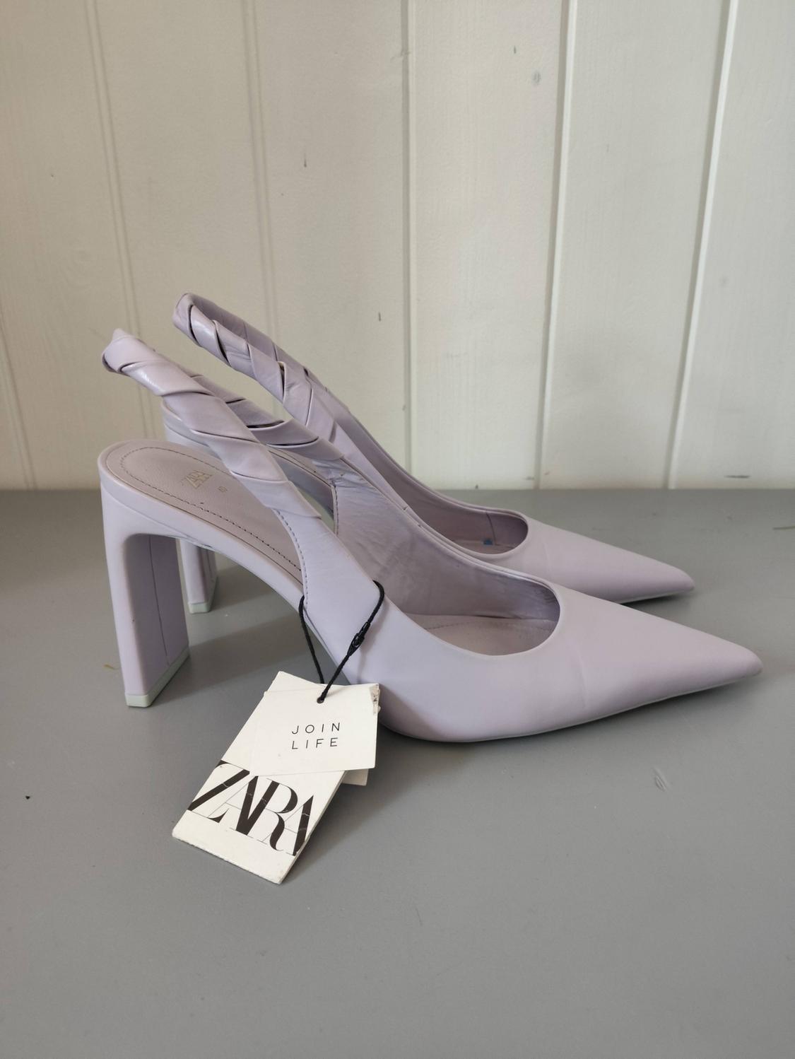 Lilac high-heeled shoes with a braided slingback strap and pointed toe on a grey surface. Label with text JOIN LIFE ZARA.
