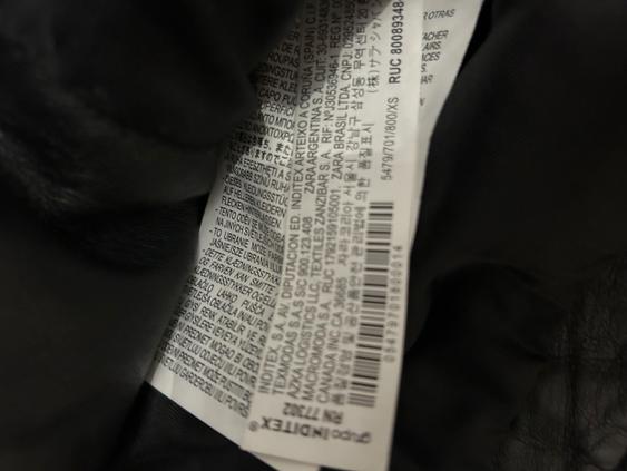 Clothing label with multi-language text and a visible barcode, on a dark fabric background.