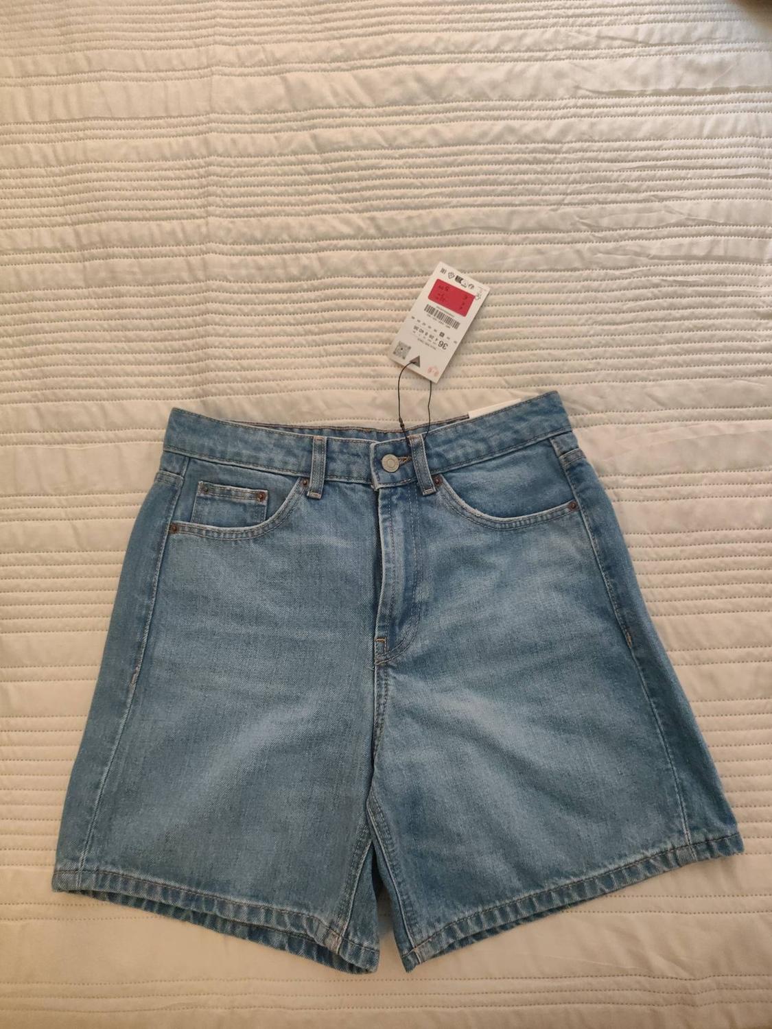 Light blue denim shorts, size 36 label, on a ribbed white bedspread. Casual and relaxed style.