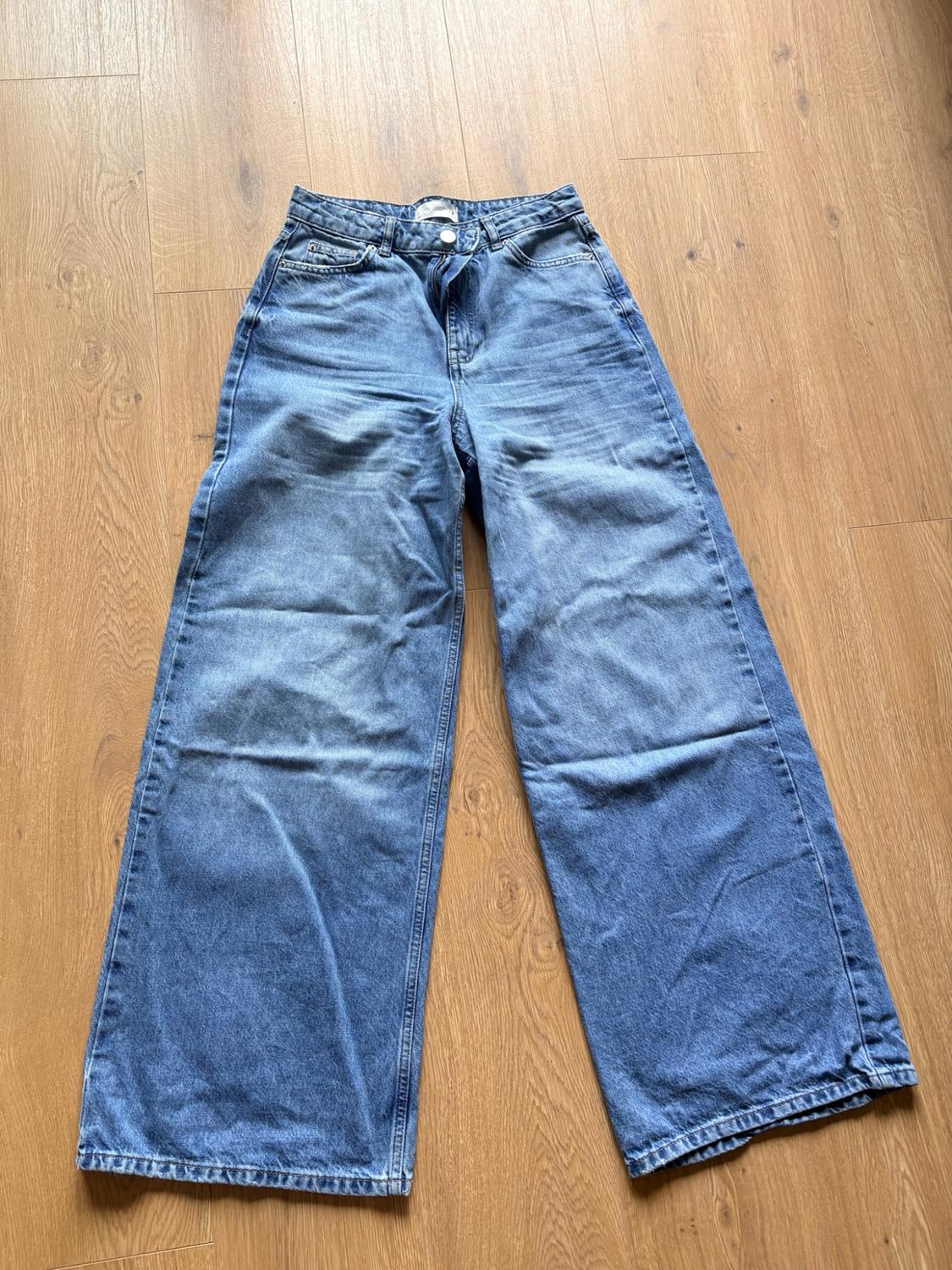 Wide-leg blue jeans laid out on a light wooden floor. Casual, relaxed style.