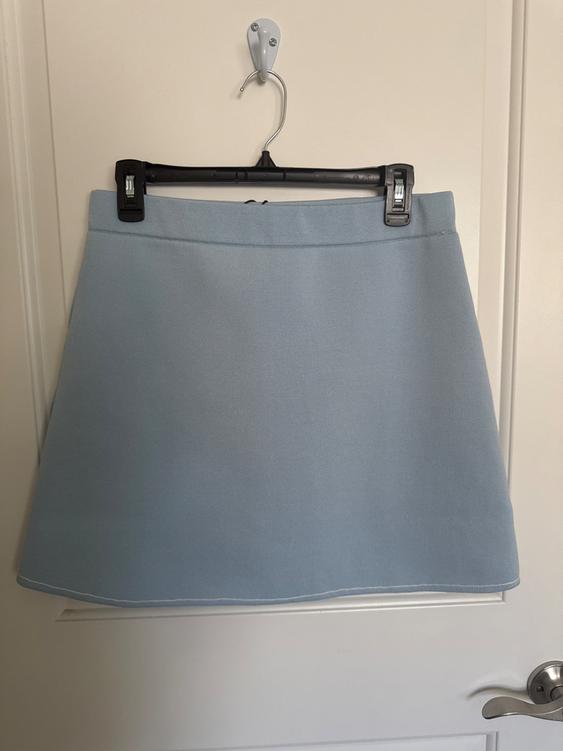 Light blue skirt hanging on a black hanger over a white door. The skirt has a simple design and a straight cut.