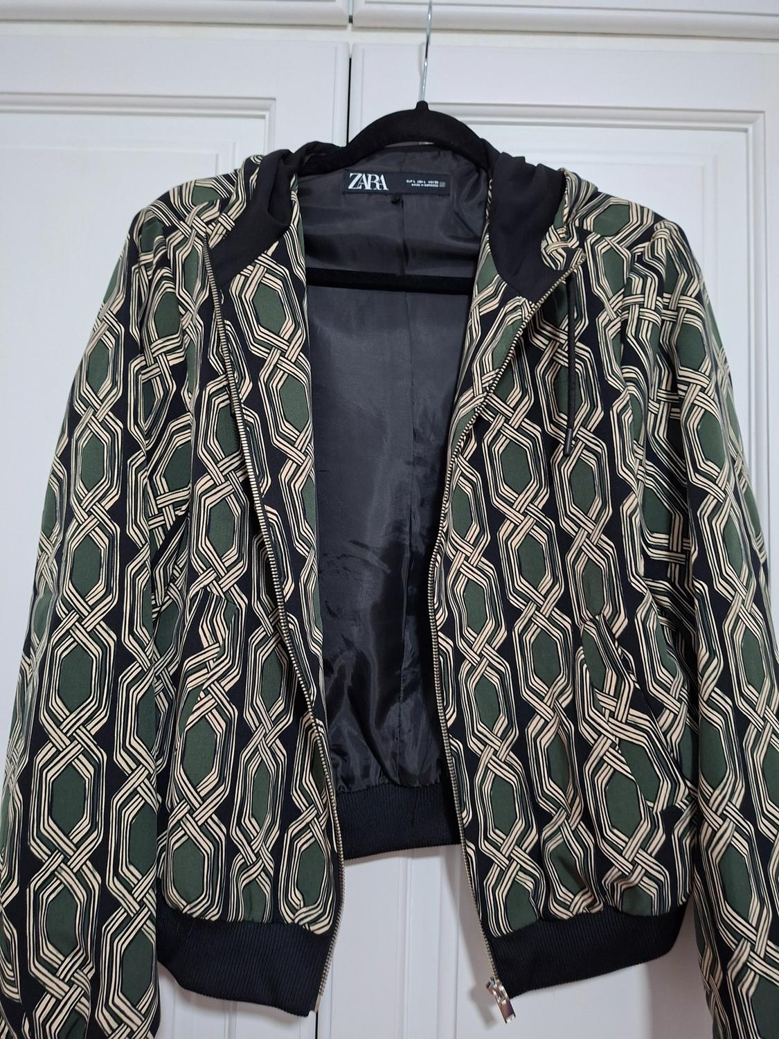 Jacket hanging with a geometric print in green and beige tones. Black interior. Visible label with the text "ZARA".