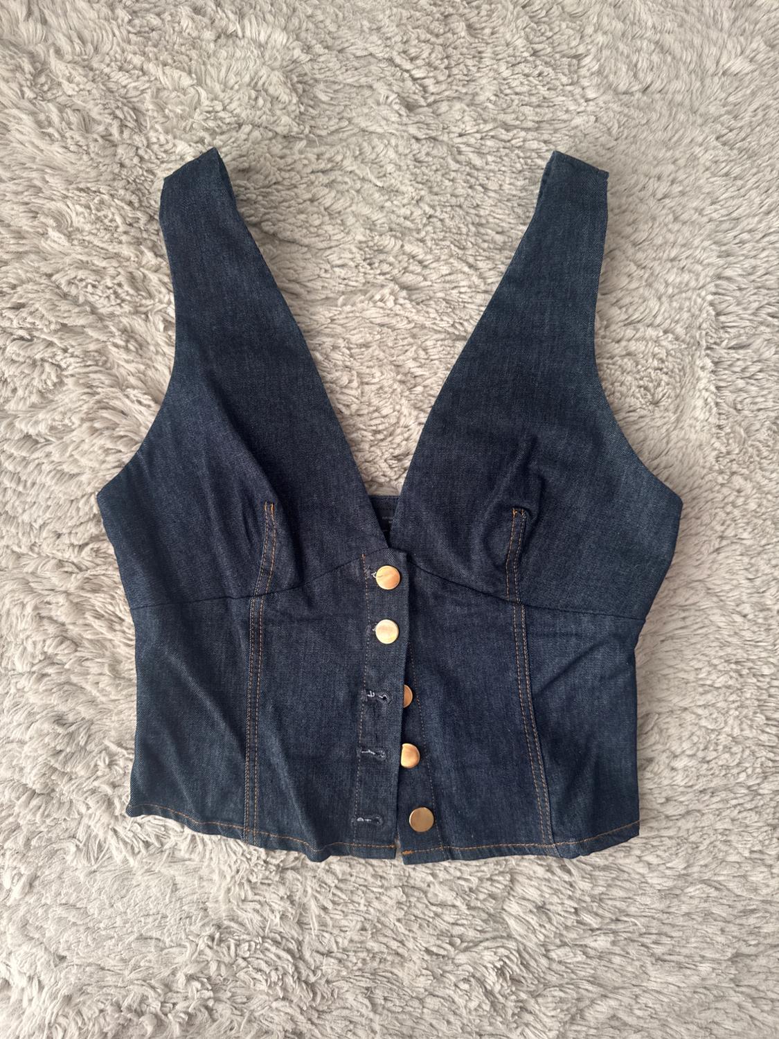 Dark blue denim top with a V-neck and gold-coloured front buttons, lying on a soft grey faux-fur rug.