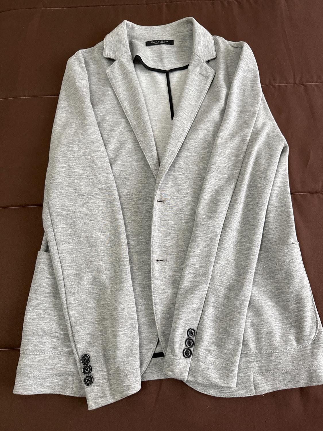Light grey jacket with lapels and black buttons, on a brown surface. Visible label: "Zara Man".