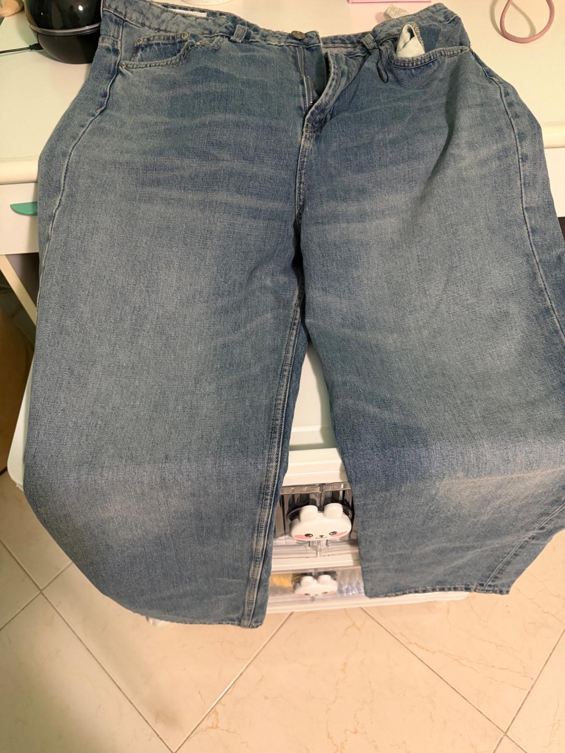 Distressed blue jeans laid out on a white surface, with storage drawers visible underneath.