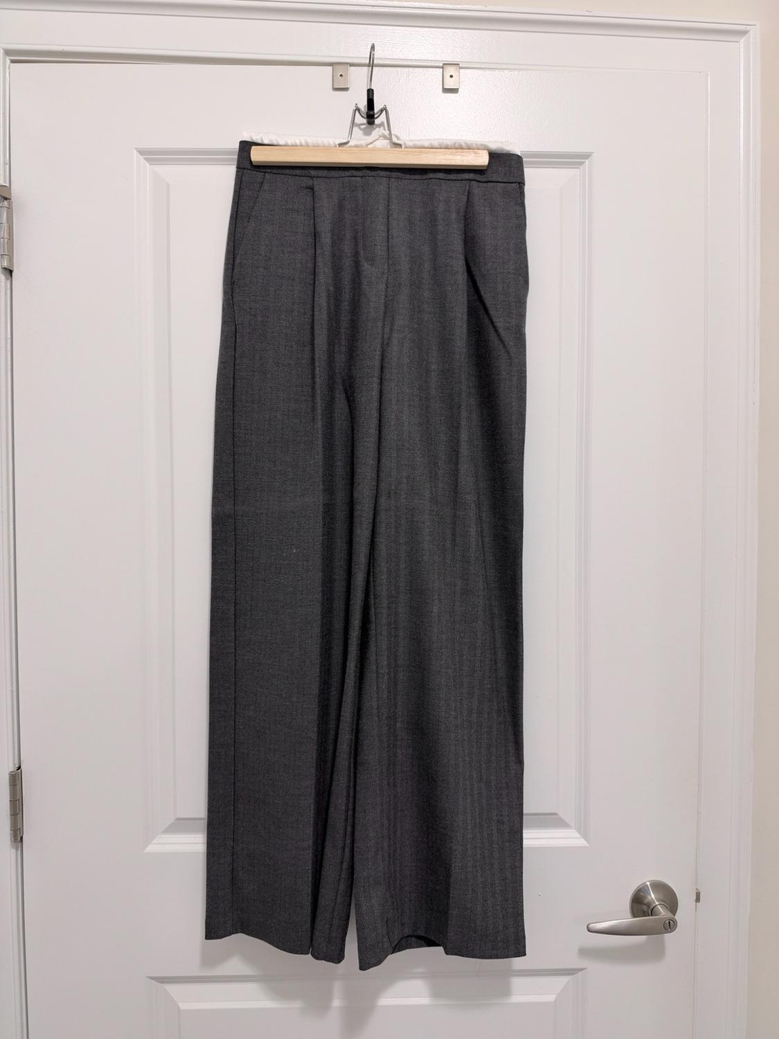 Dark gray wide-leg trousers hanging on a wooden hanger from a white door.