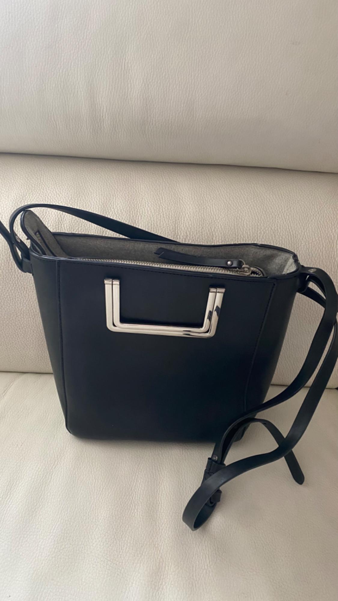 Black handbag with long handles and silver metallic details on a white sofa. Modern and elegant design.