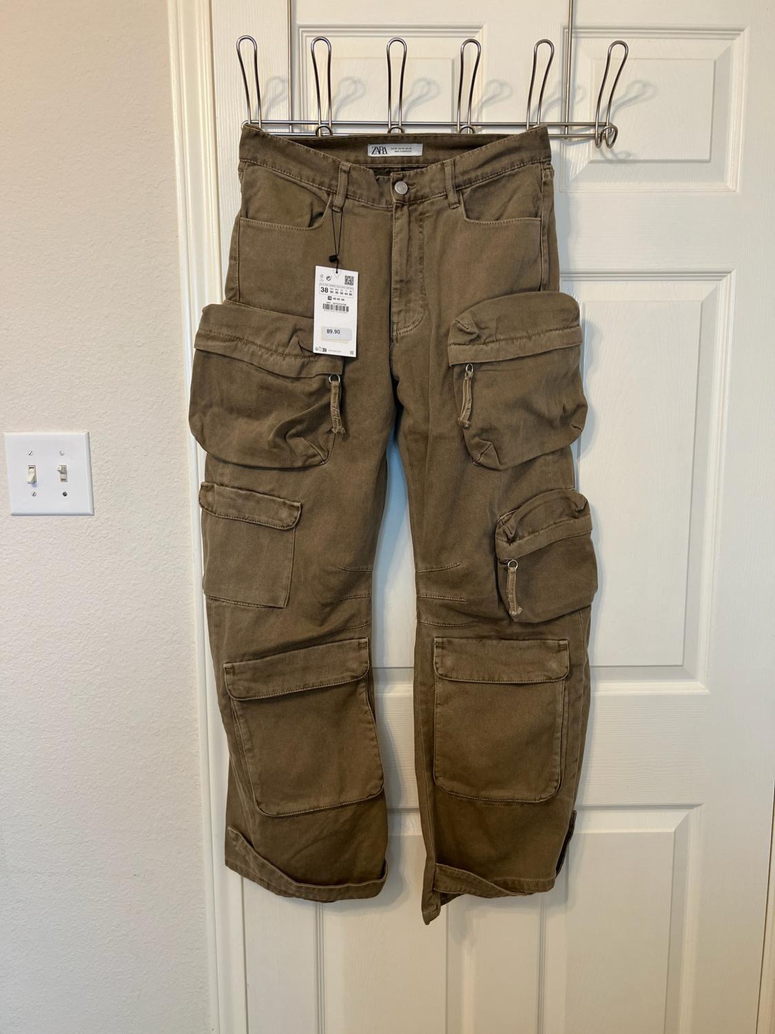 Brown cargo trousers with multiple pockets hanging on a white door. Visible ZARA tag with the text 38 and 89.90.