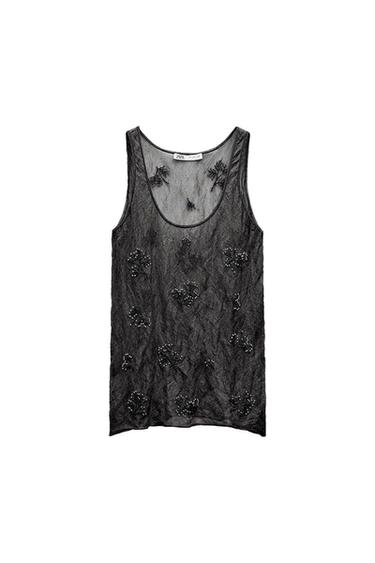 Black sheer sleeveless top with floral embroidery and bead details. White background. Visible tag on the collar.
