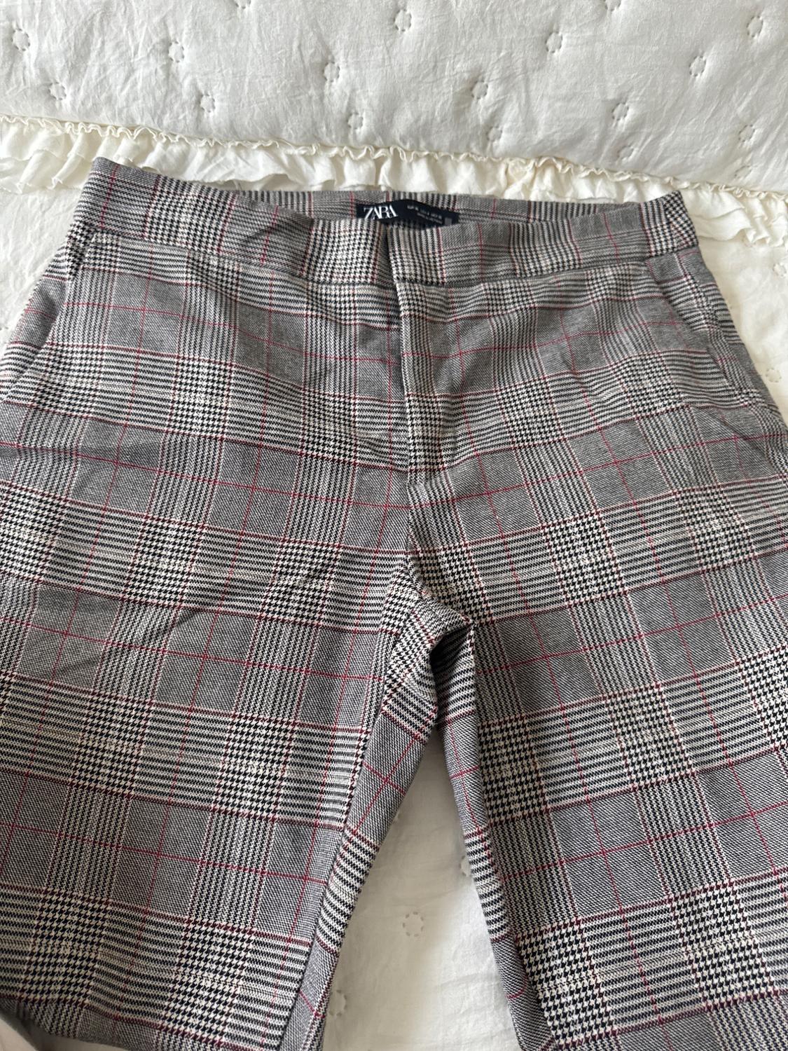 Grey checked trousers with red and black lines on a white bedspread. Visible label on the waistband.
