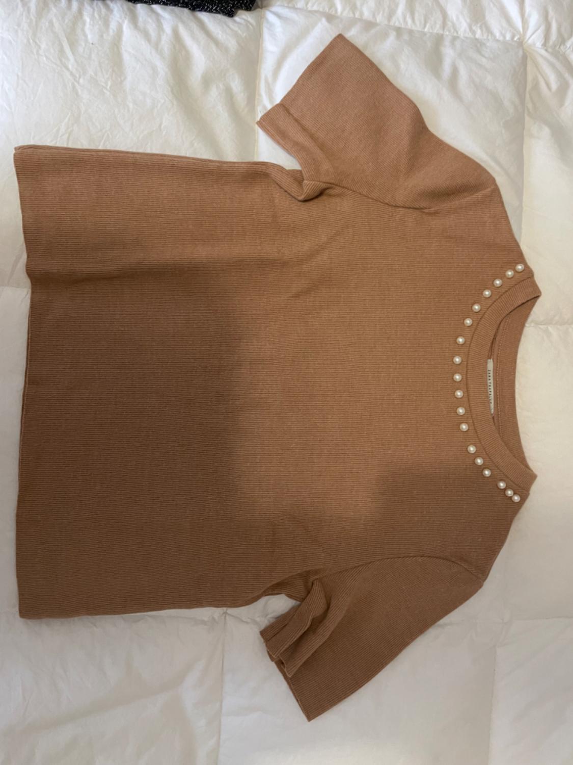 Brown short-sleeved T-shirt with pearls on the collar, on a padded white surface.