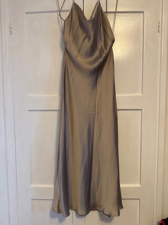 Beige satin dress hanging on a white door, with thin straps and V-neck.