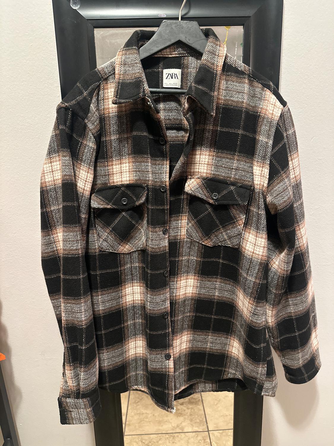 Checked shirt in dark shades hanging on a black hanger in front of a mirror. Visible label with the text "ZARA".